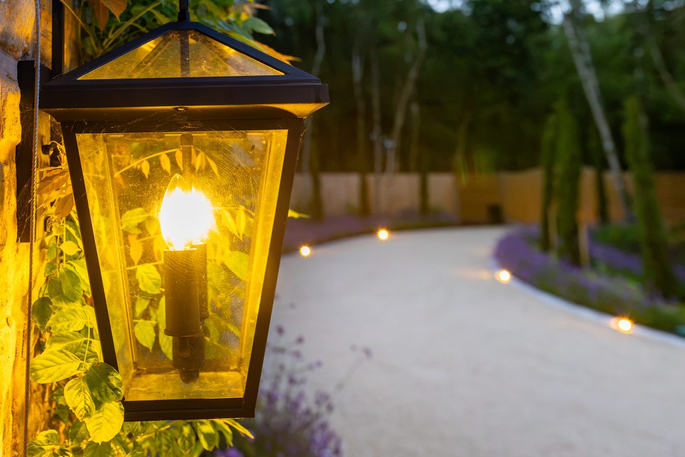 A lantern glowing over the lit garden path at Warren House at night