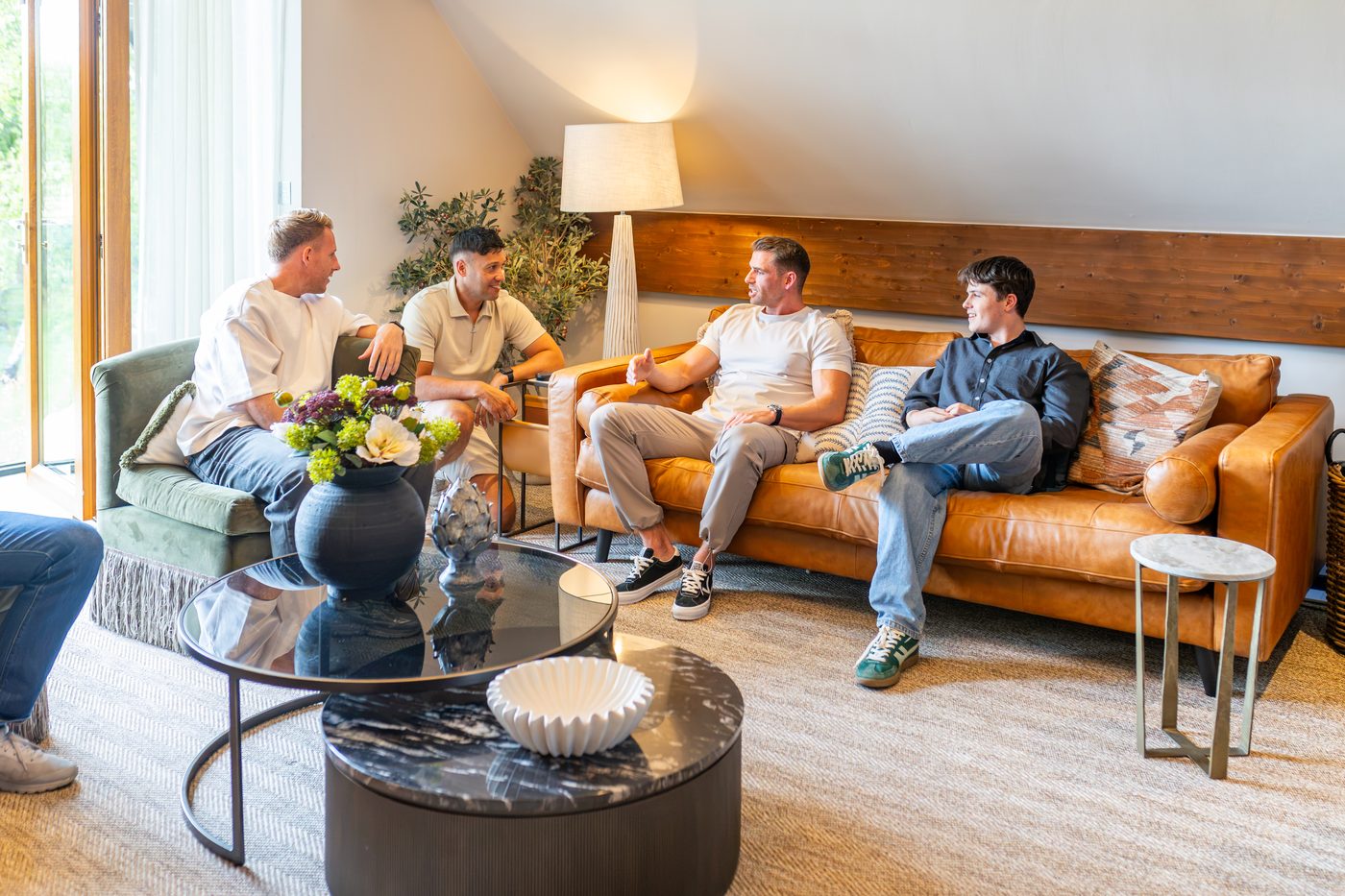 Friends relaxing on the tan leather sofas under the vaulted lounge ceiling at Warren House