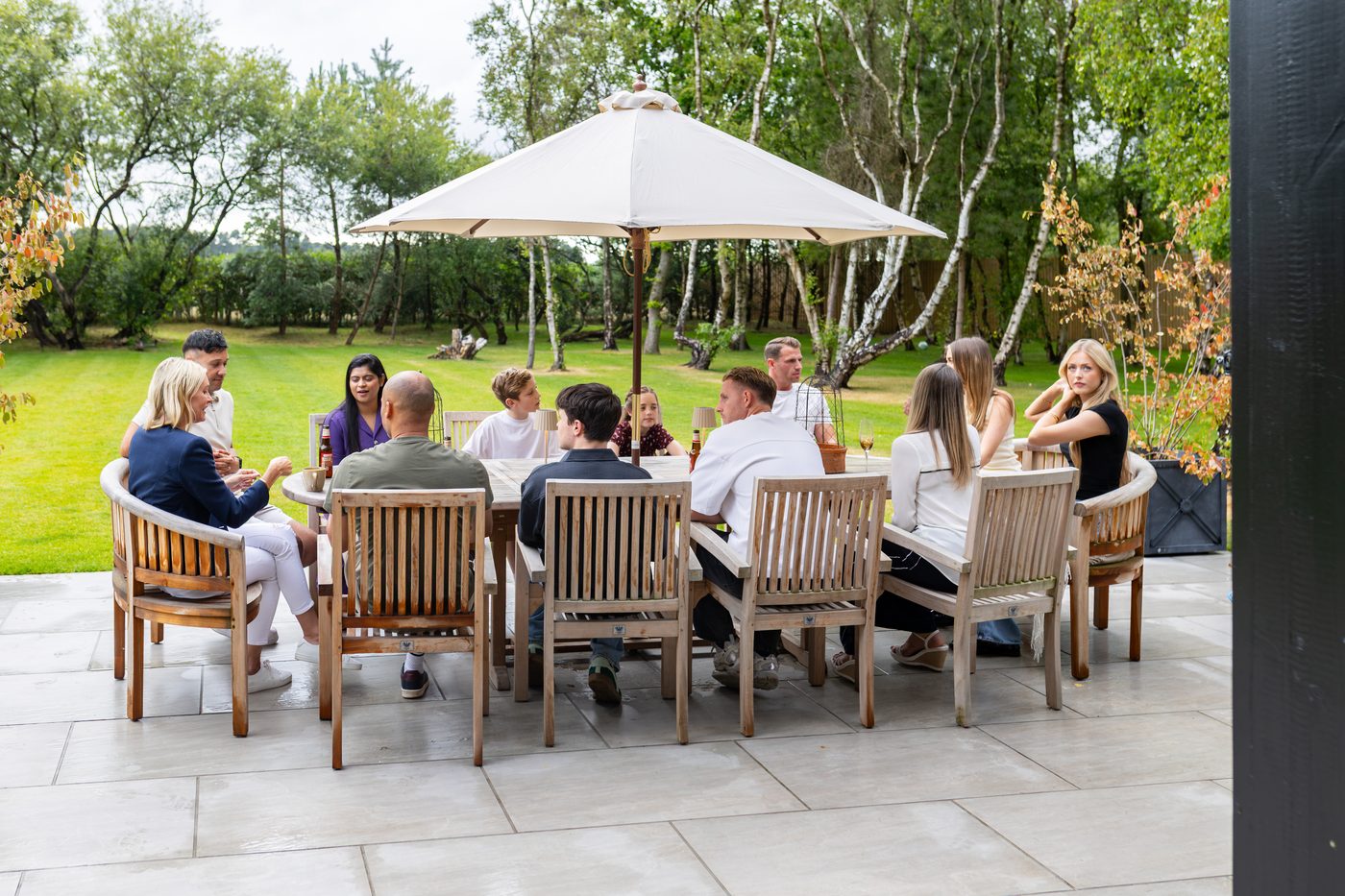 The whole group laughing around the patio table under the parasol at Warren House